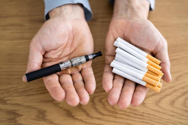 Stock image of man holding an e-cig in one hand and cigarettes in the other. 