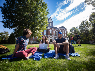 Candid photo of UK students sitting outside on the grass and talking. 