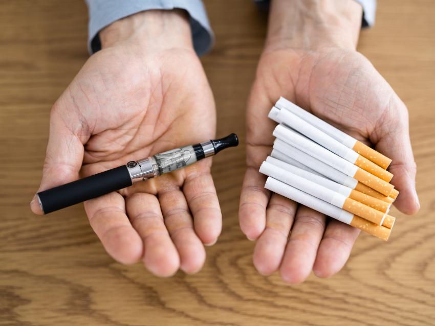 Stock image of man holding an e-cig in one hand and cigarettes in the other.