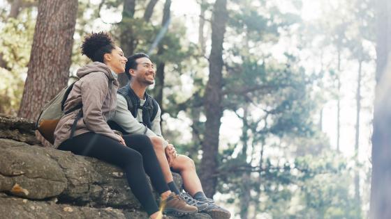 Stock photo of a couple sitting on a rock in nature, enjoying the outdoors. 